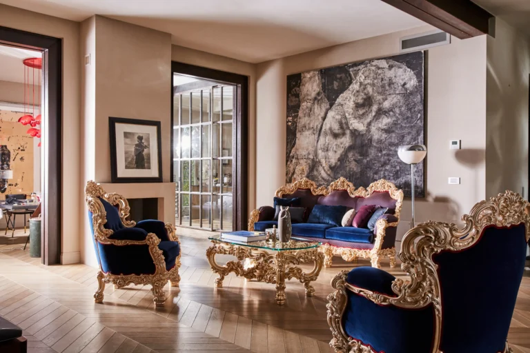 Living room with a set of baroque furniture — blue velvet armchairs and a sofa with gilded frames, a glass coffee table, and a monumental abstract wall panel.
