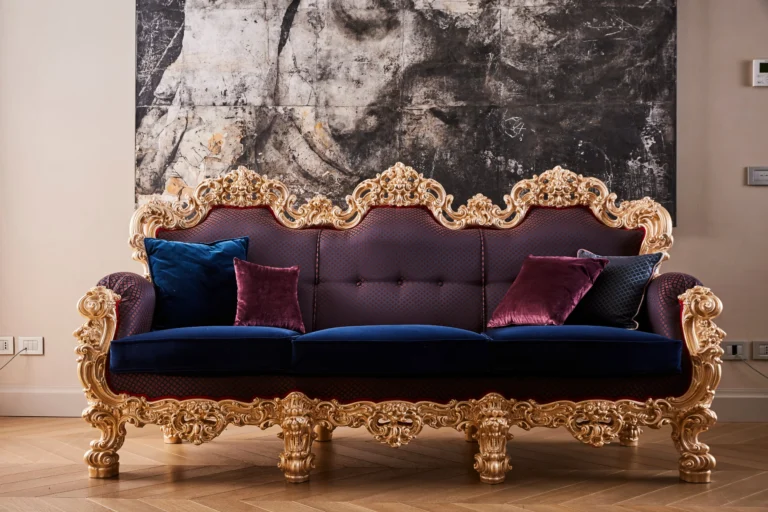 A monumental three-seat baroque-style sofa with purple-blue velvet upholstery and a massive gilded carved frame, set against an abstract painting background.