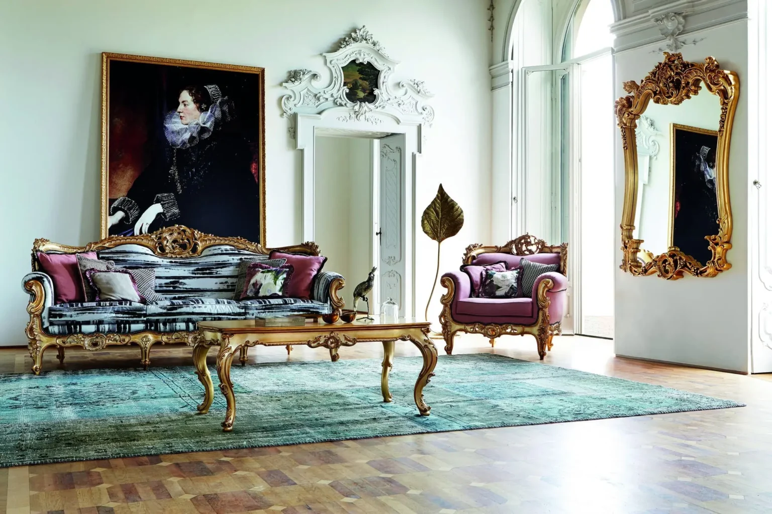 Luxurious baroque-style living room with a gilded sofa in silver fabric, a dusty rose velvet armchair, a golden coffee table, a turquoise carpet, and a gilded framed mirror.