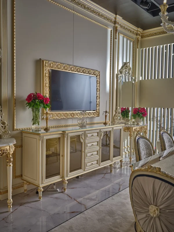 Classic ivory-colored sideboard with gold details, glass doors and drawers, and a TV in a golden frame above it.