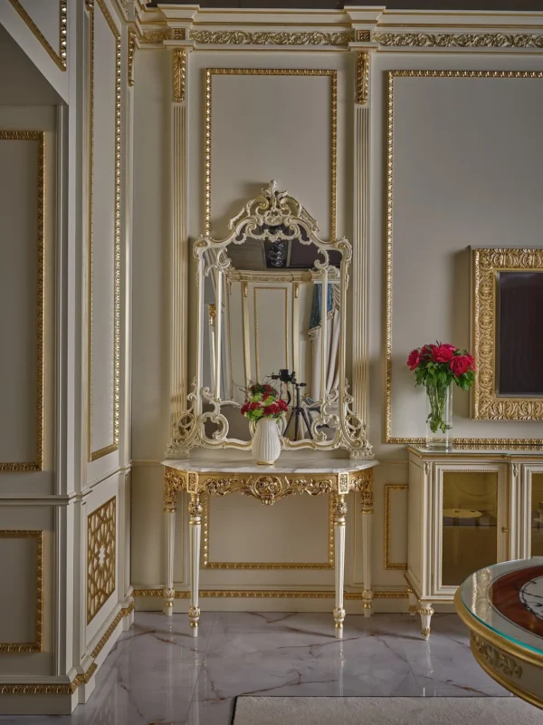 Elegant console table with a marble top and a gilded carved mirror, set against a wall with decorative paneling and gold moldings.
