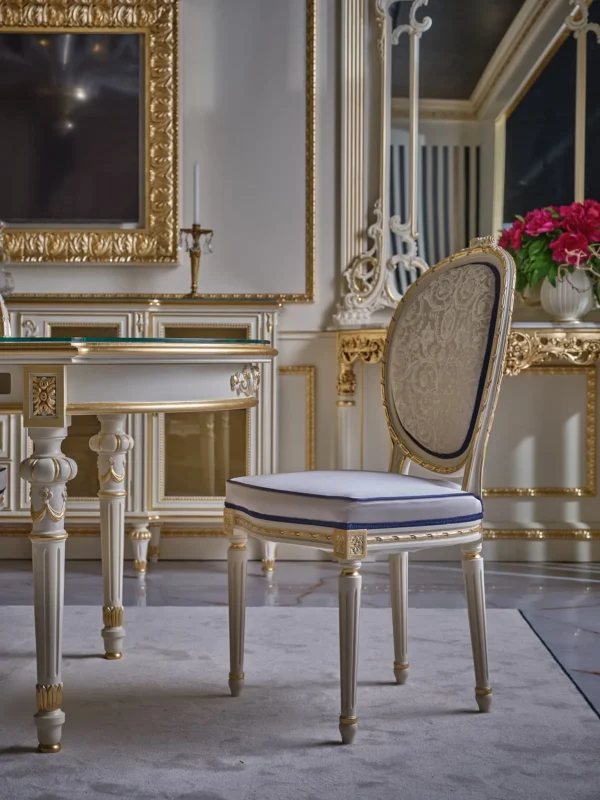 Classic Louis XVI style chair with a white lacquered frame, gold accents, a damask-patterned backrest, and a white seat with blue piping.